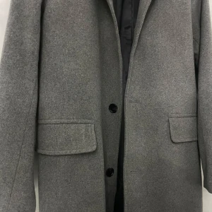 Grå kappa från H&M - Säljer en stilren grå kappa från H&M i storlek M. Den har en klassisk design med knappar framtill och långa ärmar. Perfekt för höst och vinter, och ger en elegant touch till vilken outfit som helst. Kappan är i mycket bra skick och redo för nya äventyr! Oanvänd 