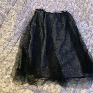 Svart glittrig kjol från Lindex - Säljer en superfin svart glittrig kjol från Lindex i storlek 134/140. Perfekt för festliga tillfällen med sitt skimrande material. Kjolen har en elastisk midja för extra komfort. Passar perfekt till fest! 