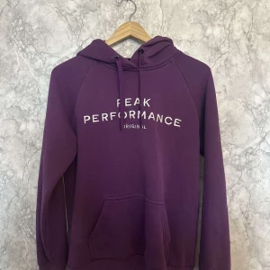 Lila hoodie från Peak Performance - Säljer en snygg lila hoodie från Peak Performance i storlek M. Den har en klassisk design med en stor ficka fram och justerbar huva. Perfekt för kyliga dagar och ger en avslappnad stil. Passar både till vardags och för mysiga hemmakvällar.