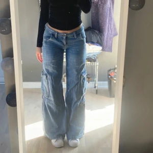 Blå jeans från BDG Urban Outfitters - Säljer ett par snygga blå jeans från BDG Urban Outfitters. De har en loose fit och är högmidjade med cargofickor på sidorna. Perfekta för en avslappnad stil och passar till både vardag och fest.
