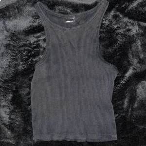 Svart ribbad linnetopp från Gina Tricot - Säljer en stilren svart ribbad linnetopp från Gina Tricot. Perfekt för sommardagar eller som ett basplagg i garderoben. Toppen är ärmlös och har en tight passform. Aldrig använd 