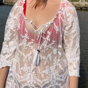 Vit spetsblus med knytband - Säljer en superfin vit spetsblus med trekvartsärmar och knytband framtill. Perfekt för en dag på stranden eller en somrig utflykt. Blusen är genomskinlig och har vackra broderade detaljer som ger en romantisk känsla.