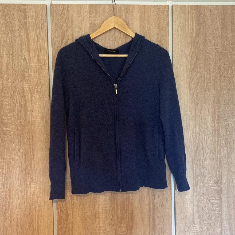 Säljer en snygg och bekväm mörkblå 100% kashmir zip hoodie från Lawrence grey. Den har en dragkedja framtill och är perfekt för både höst och vår. Tröjan är långärmad och gjord i kashmir som håller dig varm. Perfekt för en avslappnad stil!. Neuletakit & Villapaidat.