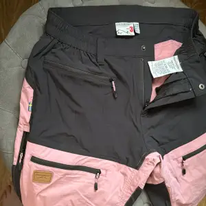 Säljer ett par snygga och funktionella shorts från Swedemount. Stl 38. De är svarta med rosa detaljer och har flera praktiska dragkedjefickor. Perfekta för utomhusaktiviteter och äventyr. Shortsen har en elastisk midja för extra komfort. Ordpris 700