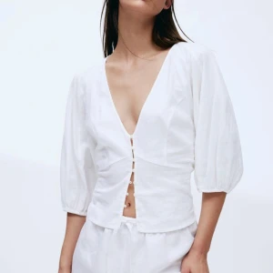 Vit blus med knappar - Säljer en superfin vit blus med knappar framtill. Den har en v-ringad design och trekvartsärmar som ger en luftig känsla. Perfekt för både vardag och fest!