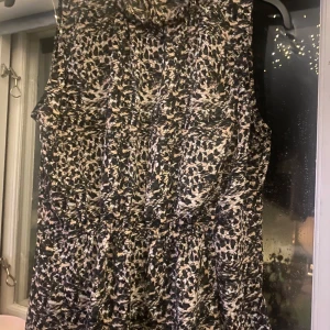 Mönstrad ärmlös klänning från H&M - Säljer en snygg ärmlös blus från H&M med ett coolt mönster i svart, beige och vita toner. Perfekt för både vardag och fest! Klänningen har en bekväm passform och är i storlek L. Passar perfekt för sommarens alla tillfällen.