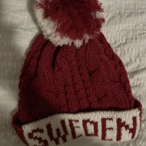 Röd stickad mössa med texten 'Sweden' - Säljer en superfin röd stickad mössa med texten 'Sweden' i vitt. Den har en fluffig tofs på toppen som är röd och vit. Perfekt för kalla vinterdagar! Använd ett fåtal gånger så i bra skick. Köp via KÖP NU 💕