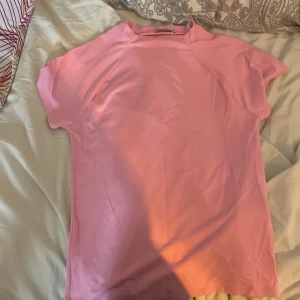 Rosa t-shirt från Zara - Säljer en söt rosa t-shirt från Zara i storlek L. Den är kortärmad och perfekt för sommardagar. Materialet känns mjukt och bekvämt, vilket gör den idealisk för vardagsbruk. Passar bra till jeans eller shorts för en avslappnad look.