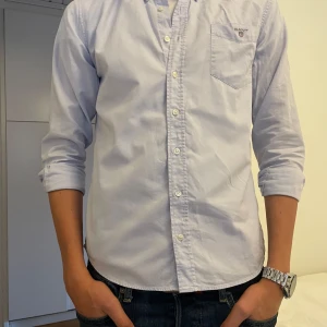 Ljusblå skjorta från GANT - Säljer en stilren ljusblå skjorta från GANT i mycket bra skick. Skjortan är i storlek 170cm men passar även på mig som är 180. Skjortan har långa ärmar och en klassisk krage med knappar framtill. Perfekt för både vardag och fest! Den har en bröstficka med GANT-loggan broderad ovanför. Passar perfekt för en avslappnad men ändå uppklädd look. 