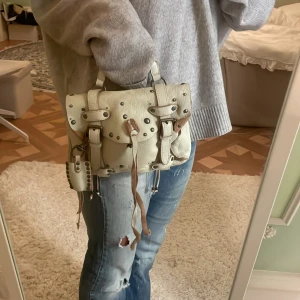 Beige axelväska i skinn - Säljer en superfin beige axelväska i skinn med coola detaljer som nitar och spännen. Väskan är från Polo Ralph Laurent i befintligt skick🤍