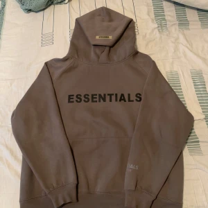 Brun hoodie från Essentials - Säljer en snygg brun hoodie från Essentials, perfekt för en avslappnad stil. Den har en stor logga på framsidan och är gjord i mjukt material för extra komfort. Passar perfekt till höst och vinter. 🧥