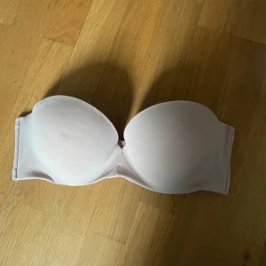 Beige axelbandslös bh - Säljer en stilren beige axelbandslös bh i mycket bra skick. Perfekt för toppar och klänningar utan axelband. Den har en slät yta och ger bra stöd. Passar perfekt för både vardag och fest!