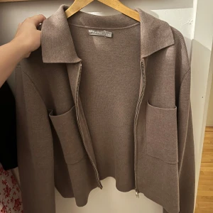 Beige kofta från Åhléns  - Säljer en superfin beige kofta från Åhléns  i mycket bra skick. Den är stickad och har en dragkedja framtill samt två stora fickor. Perfekt för höst och vår när det är lite kyligt ute. Passar både till vardags och lite mer uppklädda tillfällen. Storlek M .