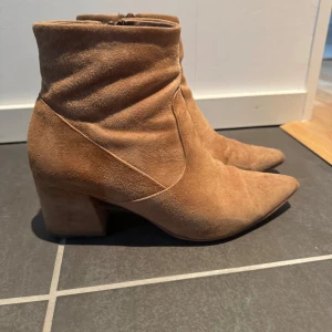 Bruna mocka boots med klack - Säljer ett par snygga bruna boots i mocka med klack och spetsig tå. Perfekta för höst och vår, de har en dragkedja på sidan för enkel på- och avtagning. De är i mycket bra skick och passar både till vardags och fest. Superbekväma och stilrena!