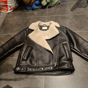 Svart skinnjacka med foder från Zara - Säljer en snygg svart skinnjacka från Zara med mjukt beige foder. Jackan har snygga detaljer längst ner. Och är perfekt för vintern❤️ det är storlek 164 från barnstorlek men skulle säga att den passar nån med XS-S. Jag köpte den för 550kr