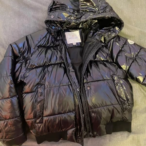 Svart pufferjacka från Moncler - Säljer en snygg svart pufferjacka från Moncler hyfsat bra sick finns lite skavanker på insidan . Jackan har en glansig yta och är perfekt för kalla dagar. Den har en huva och stängs med dragkedja och knappar. Supervarm och stilren!