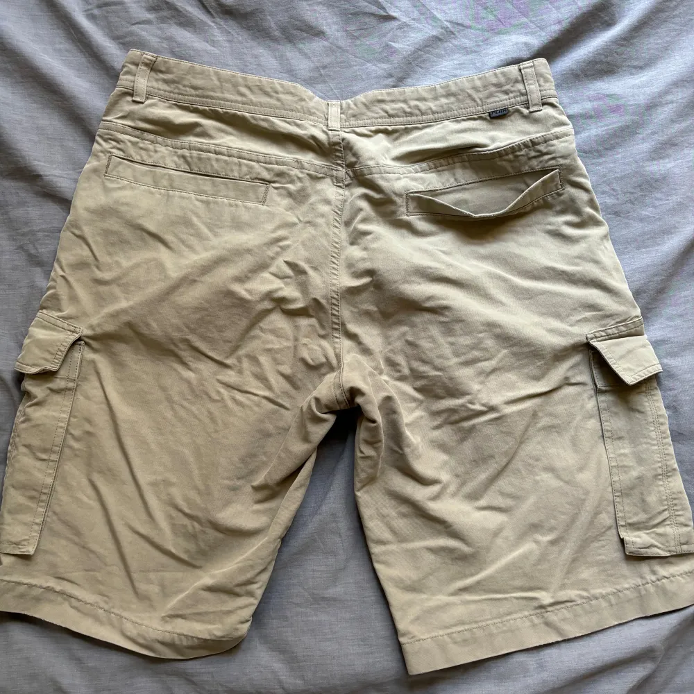 Beige vintage cargo shorts från Peak Performance, flitigt använda men väl omhändertagna. Naturlig slitage vid benöppning (se bild) Köpta i vintagebutik för ca 200kr, men säljer då de ej kommit till använding (L: 55cm, W: 46cm, Innersöm: 28cm, Benöppning: 30cm). Shorts.