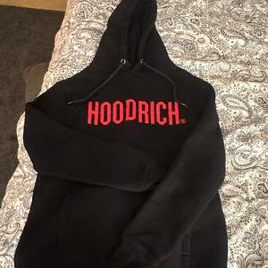 Säljer en svart hoodie från Hoodrich i storlek XS. Den har en stor röd logga på bröstet och en klassisk känguruficka. Perfekt för en casual look eller att mysa i hemma. Huvan har justerbara snören för bästa passform. 🖤