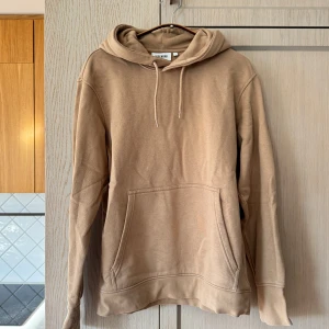 Beige hoodie från Weekday - Storlek S - Säljer en snygg beige hoodie från Weekday i mycket bra skick. Den är supermjuk och perfekt för höst och vår. Har en klassisk känguruficka och justerbar huva med dragsko. Perfekt för en avslappnad stil!