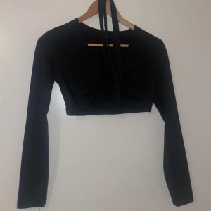 Svart långärmad croppad topp - Snygg svart croppad topp från Shein i storlek S. Den har långa ärmar och en cool knytdetalj framtill med en ring som ger en unik look. Perfekt för en utekväll eller fest!