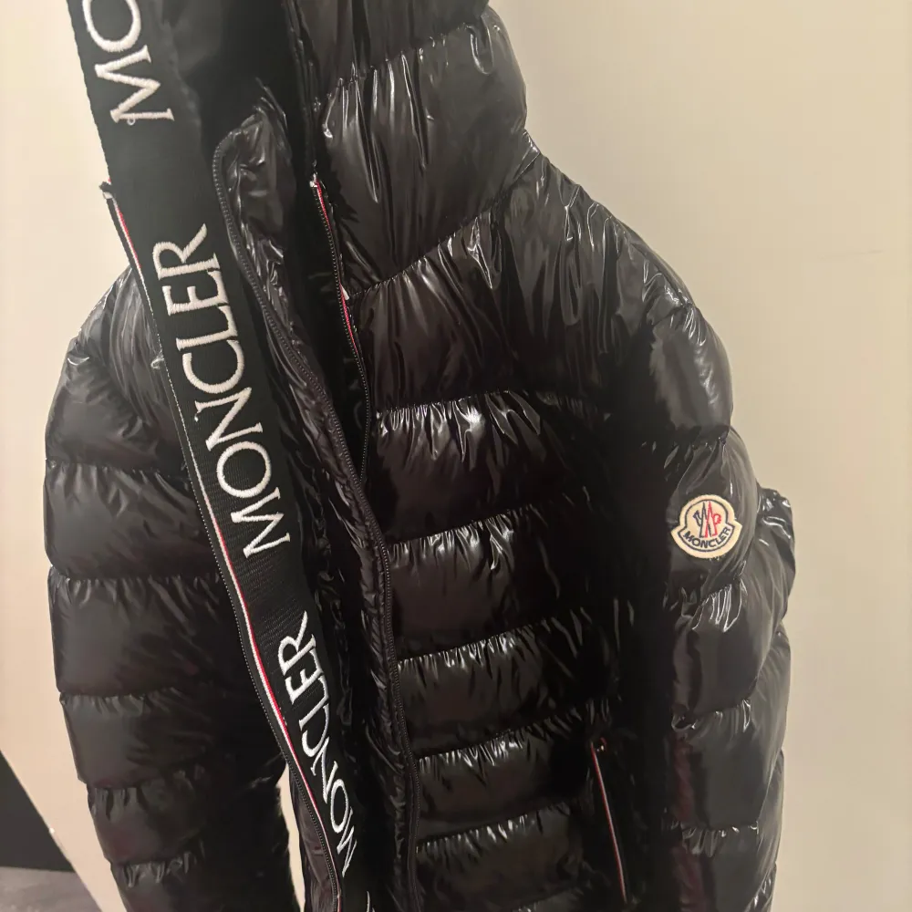 Säljer en snygg svart pufferjacka från Moncler i mycket bra skick. Jackan har en glansig finish och är perfekt för vintern. Den har en dragkedja framtill och Moncler-logga på ärmen. Huvan är fodrad och har Moncler-tryck. Perfekt för att hålla sig varm och stilren i kylan!. Jackor.