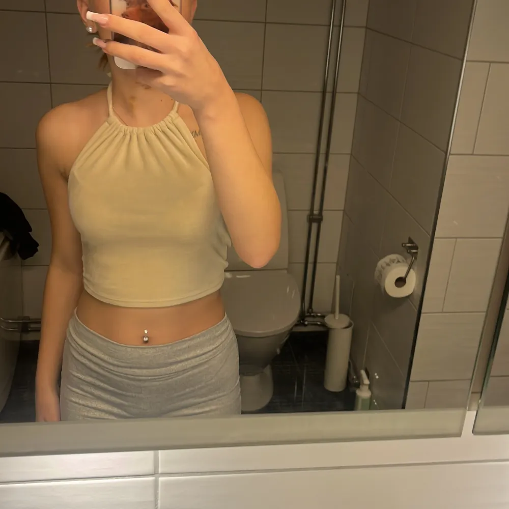 Säljer en snygg beige halterneck topp i croppad stil. Perfekt för sommaren med sin ärmlösa design och knytning i nacken. Toppen är i bra skick och passar perfekt till både vardag och fest. Superfin att matcha med höga jeans eller kjol!. Toppar.