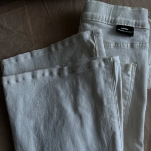 Vita utsvängda jeansbyxor från Denim - Säljer ett par snygga vita jeansbyxor från Denim. De är i bra skick och perfekta för både vardag och fest. Byxorna har en klassisk design med normal passform och är tillverkade i bomull för en skön känsla. Passar perfekt till vår och sommar!