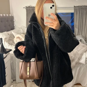 Svart teddyjacka med dragkedja - Prislappen kvar aldrig använd helt slutsåld !!!Mysig svart teddyjacka perfekt för kalla dagar. Den har en hög krage och stängs med dragkedja. Jackan är oversized och har långa ärmar med snygga detaljer i form av svarta band. Perfekt för höst och vinter! 