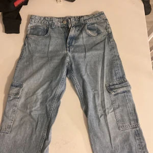 Blå cargobyxor loosefit från H&M - Säljer ett par blå cargobyxor från H&M i loose fit med justerbar midja och raka ben. Perfekta för en avslappnad stil med praktiska fickor på sidorna. Byxorna är i bra skick och passar både till vardags och annat.