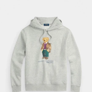 Polo Ralph Lauren Hoodie - En grå huvtröja med en stor björn på framsidan. Huvan är grå och har en dragsko. Tröjan har en ficka på magen. Tröjan är i gott skick.
