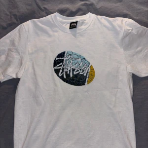 Stussy Mosaic Tile T-Shirt - En vit T-Shirt från Stussy med logo-tryck i keramik/mosaic liknande mönster, köpt för ca 800kr 2022 och har endast kommit till användning två gånger och säljer därför. En minimal defekt förekommer som är en litet grönt streck vid tröjans krage, men är knappt synlig, Köpt i butik och har därför ej kvitto tillgängligt