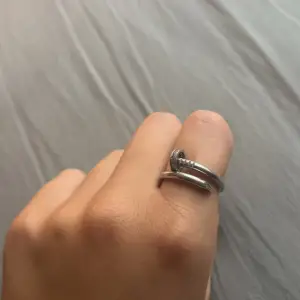 Säljer en cool silverfärgad ring med en unik design som ser ut som en böjd spik. Ringen har en slät yta och en del av ringen är dekorerad med små glittrande stenar. Perfekt för att ge din outfit en edgy touch!