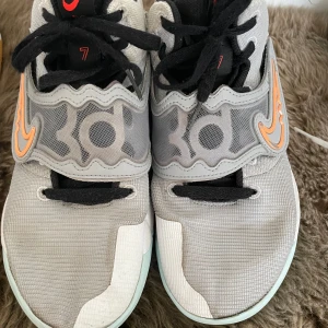 Grå Nike sneakers med orange detaljer - Säljer ett par grå Nike sneakers med coola orange detaljer och svart snörning. Skorna har en unik sula med mönster i ljusgrönt och gult, vilket ger dem en extra edge. Perfekta för både vardag och träning!