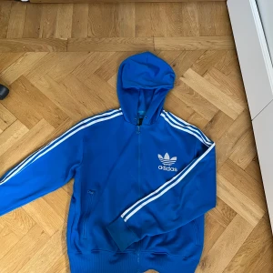 Blå adidas jacka - En välanvänd adidas jacka. Säljer för att jag inte använder längre. Det finns inget snöre kvar då jag råkat tappat bort det.