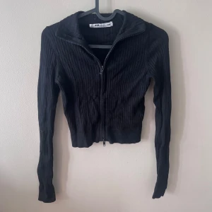 Svart ribbad tröja från FB Sister - Säljer en svart ribbad tröja från FB Sister i storlek XXS. Tröjan har en dragkedja framtill och långa ärmar, perfekt för höst och vinter. Den är både stilren och bekväm, idealisk för vardagsbruk eller en avslappnad dag ute.