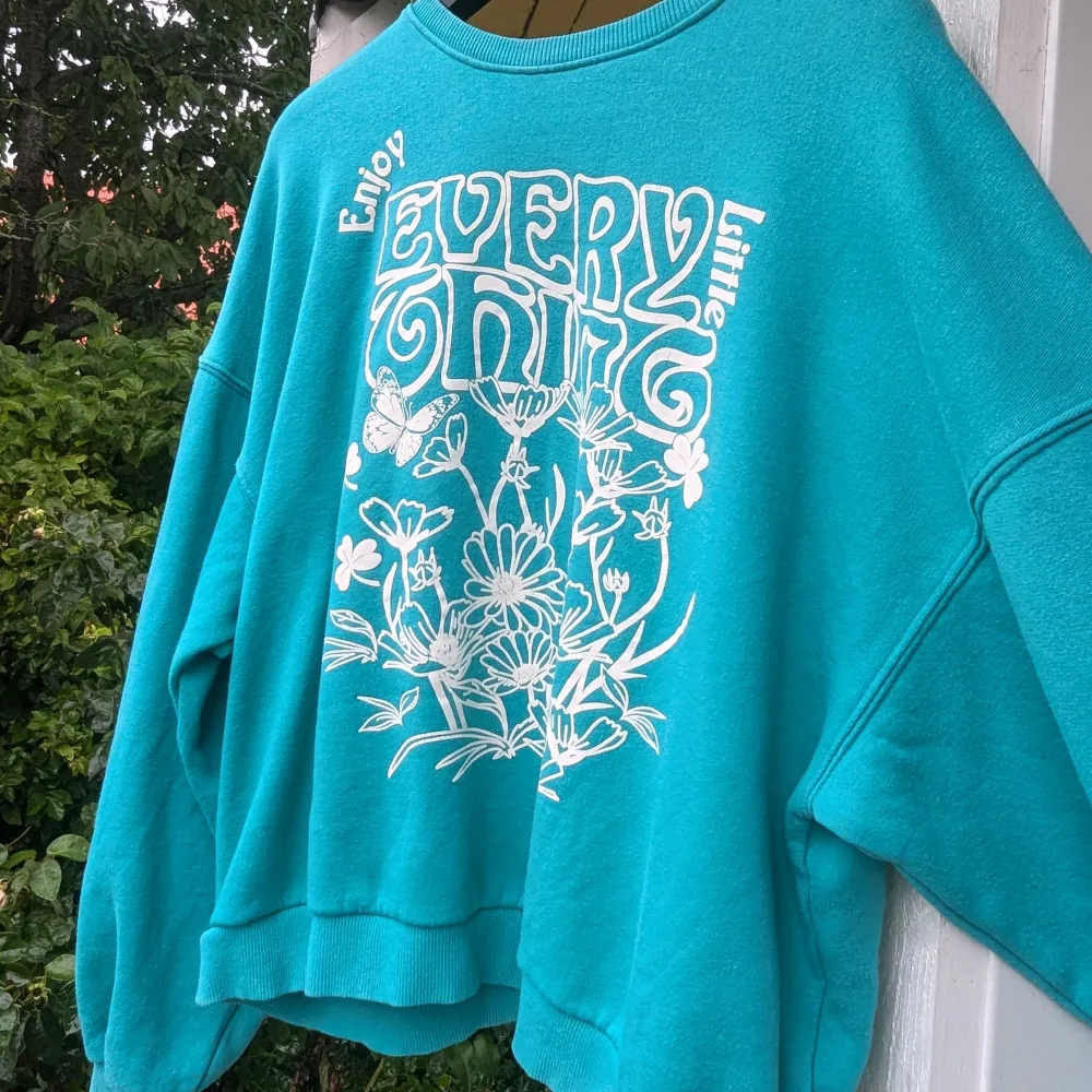 Säljer en superfin turkos sweatshirt med ett stort vitt tryck på framsidan som säger 'Enjoy Every Little Thing' och har blommor och en fjäril. Den är gjord av 97% bomull och 3% elastan, vilket gör den både bekväm och stretchig.passar S/M också . Tröjor & Koftor.