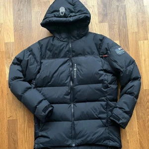 Svart pufferjacka från Sail Racing - Säljer en svart cape dow från Sail Racing i storlek Large. Jackan är i bra skick. Litet skav på texten, se sista bilden. 