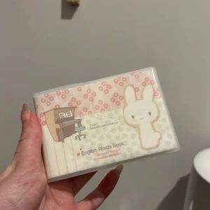 Engelska ord bok med kaninmotiv - Söt engelsk ord bok med ett kaninmotiv på omslaget. Boken har sektioner för ord, uttal, översättning och meningar. Perfekt för att lära sig nya ord och hålla koll på vokabulären. Omslaget har ett blommönster och en tecknad kanin. En anteckning som går enkelt att sudda bort, syns på sida 2