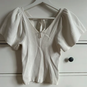 Vit ribbad topp från ONLY - Säljer en stilren vit ribbad topp från ONLY med korta puffärmar och knytning i ryggen. Perfekt för en chic och avslappnad look.