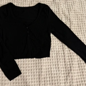 Svart ribbad kofta - Snygg svart ribbad kofta med knappar framtill. Den har en croppad design och långa ärmar, perfekt för lager på lager-stil. Om ni vill se den på, skriv gärna!