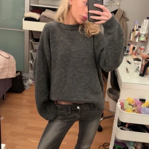 Mörkgrå stickad tröja - Säljer en mysig mörkgrå stickad tröja med en avslappnad passform. Tröjan har långa ärmar och en rund halsringning, perfekt för kyligare dagar.