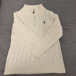 Vit stickad tröja från Polo Ralph Lauren - Säljer en stilren vit stickad tröja från Polo Ralph Lauren med kabelstickat mönster och en halv dragkedja framtill. Väldigt skön och helt oanvänd.