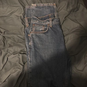 Blå jeans från Nudie Jeans - Säljer ett par klassiska blå jeans från Nudie Jeans med snygga orangea sömmar och broderade bakfickor. Perfekt för en avslappnad stil.