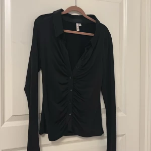 Svart långärmad blus - Svart blus med långa ärmar och knappar framtill. Den har en tight passform och materialet är stretchigt.