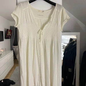 Vit klänning från Odd Molly - Charmig vit klänning från Odd Molly med korta ärmar och en söt knytning framtill. Klänningen har en smockdetalj vid bysten som ger en fin passform. Använd cirka 2 gånger så den är som ny