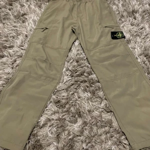 Beige cargobyxor från Stone Island - Snygga beige cargobyxor från Stone Island med flera praktiska fickor och en ikonisk logga på benet. Perfekta för en avslappnad stil med en touch av lyx.