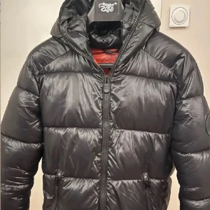 Svart pufferjacka från Save the Duck - Säljer en svart pufferjacka från Save the Duck. Jackan är 100% animal free och har en dragkedja framtill. Den är perfekt för kyligare dagar med sin vadderade design och huva. Perfekt för dig kring 170-180