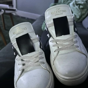 Valentino Garavani sneakers - Snygga vita Valentino Garavani sneakers med svart detalj på sidan. Skorna har snörning och är tillverkade i skinn. Perfekta för en stilren look. Storlek är 39 men passar bättre 38
