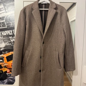 Brun kappa från Zara - Snygg brun kappa från Zara i klassisk design. Kappan har långa ärmar och stängs med knappar framtill. Perfekt för höst och vår,kanske även i vinter.Använd 2 gånger bara,köpt för 1000kr i Zara 