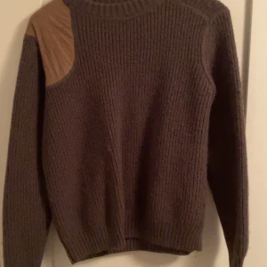 Mörk grön stickad tröja från Samsøe Samsøe - Snygg mörkgrön stickad tröja från Samsøe Samsøe med quiltade detaljer på axel och armbågar. Perfekt för kyliga dagar med sin ribbade hals och muddar.